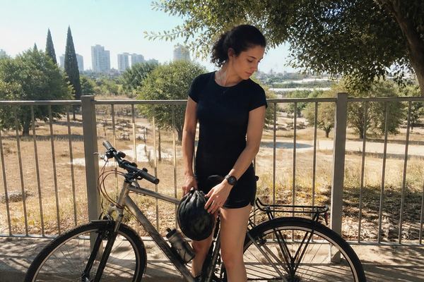 רוכב אופניים עומד ברוגע ליד האופניים שלו בחוץ, קסדה ביד, באור יום
