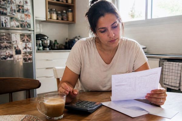 אדם יושב ליד שולחן מטבח באור יום עם כוס קפה ומחשבון, ועובר בנינוחות על תלוש שכר