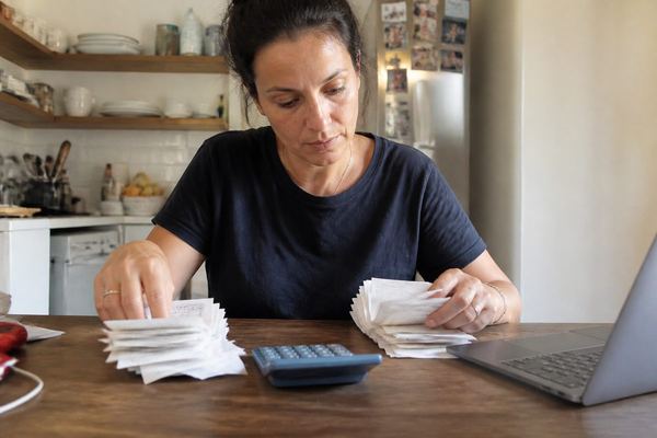 עצמאי יושב ליד שולחן מטבח עם מחשבון ומחשב נייד וממיין שתי ערימות של קבלות, באור יום