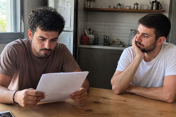שני חברים ליד שולחן מטבח באור יום, אחד קורא בעיון מסמך הלוואה והשני ממתין לידו
