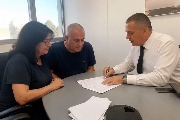 שני מבוגרים בשנות ה-50 יושבים ליד שולחן עם עורך דין ועוברים ברוגע על מסמכים, באור רך