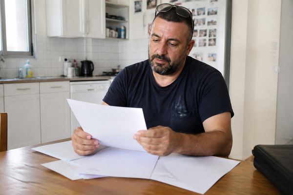 בעל מקצוע עצמאי בשנות ה-40 יושב ליד שולחן מטבח באור יום ועובר ברוגע על מסמך ביטוח