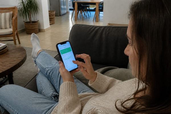 אדם יושב על ספה באור אחר הצהריים ובודק פיקדון חיסכון באפליקציית הבנק בטלפון