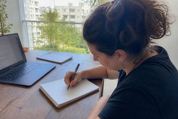 אדם יושב ליד שולחן ומצייר דיאגרמת עוגה פשוטה במחברת, מחשב נייד פתוח לצידו, באור יום