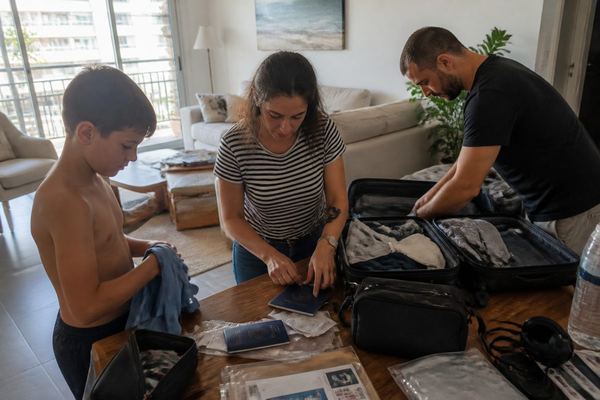 משפחה אורזת מזוודות בבית, דרכונים ומסמכים מסודרים על השולחן, אווירה רגועה באור יום