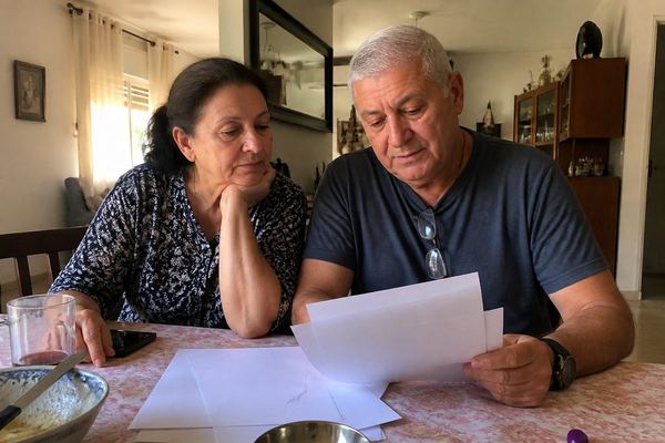 זוג מבוגר בשנות ה-60 יושב יחד ליד שולחן ועובר ברוגע על ניירות, באור חם של אחר הצהריים