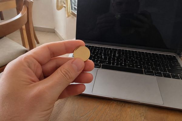 יד מחזיקה מטבע זהב קטן ופשוט ליד מחשב נייד על שולחן, באור חם בתוך הבית
